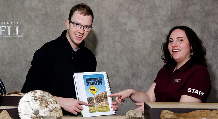 Two educators point to a book with text reading, “Dinosaur Country.”